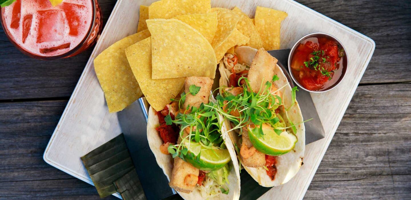 A plate of tacos and chips and a drink garnished with a lemon