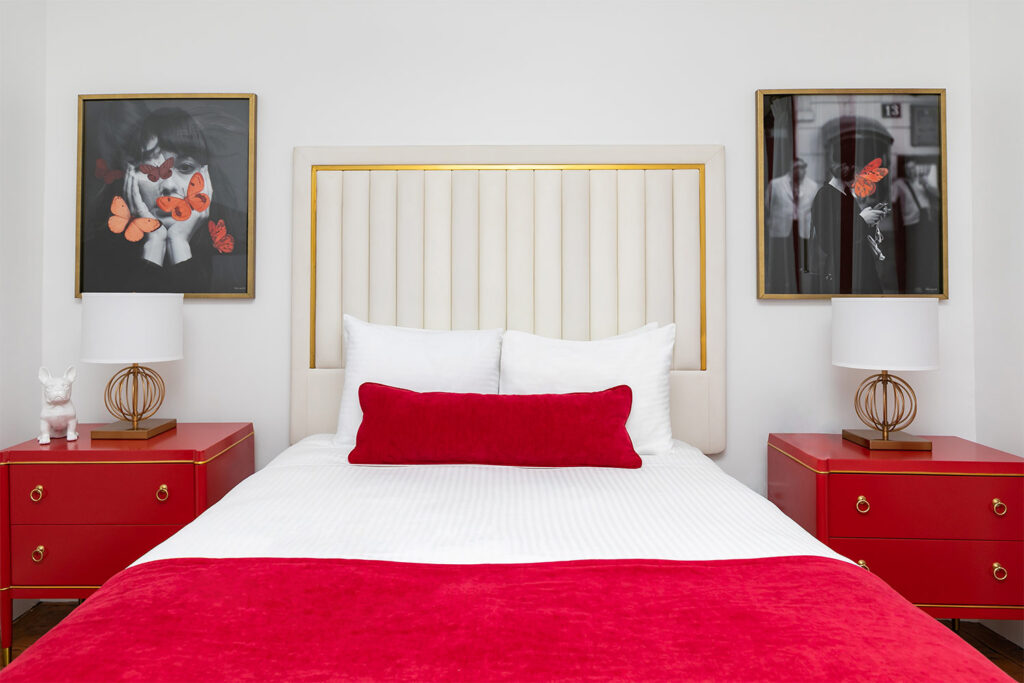 Hotel room with queen bed with white and red blankets and red bedside tables