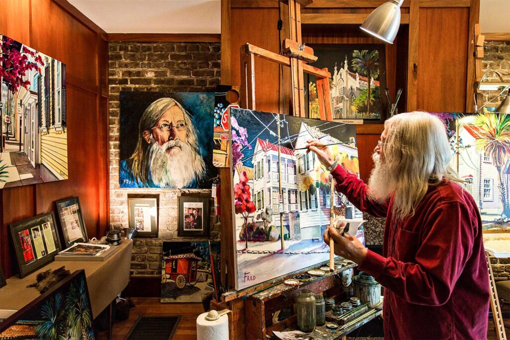 man in red shirt painting on a canvas in an artist studio