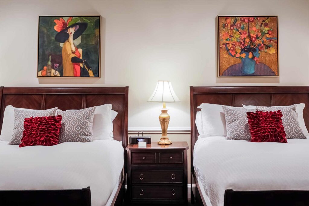 Two queen beds with red and white pillows and paintings above