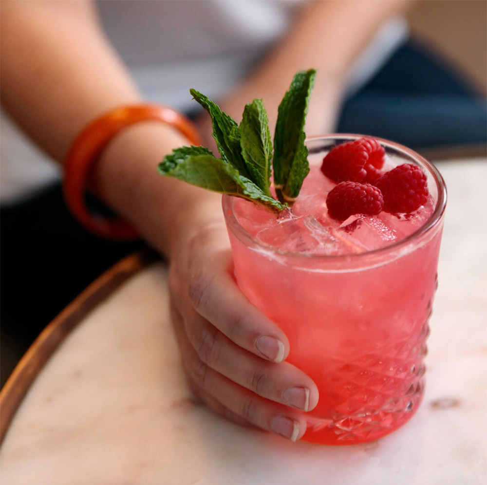 pink cocktail with mint leaves and raspberry garnishes