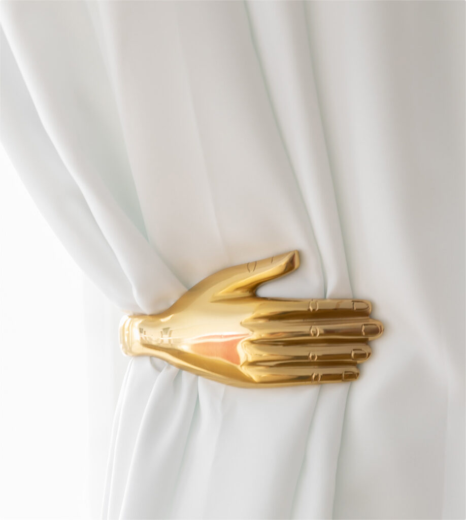Gold hand holding a white curtain